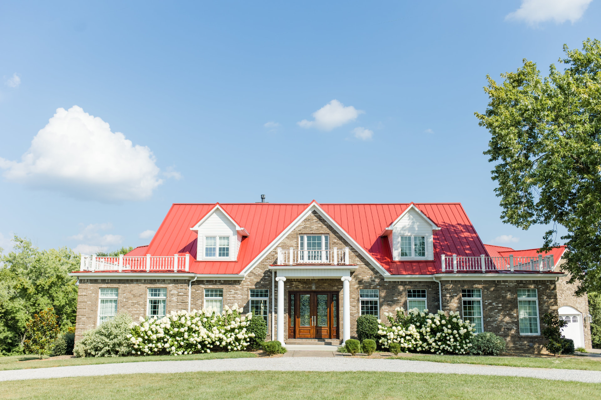 The Commonwealth, a brick home with a red roof and white hydrangeas